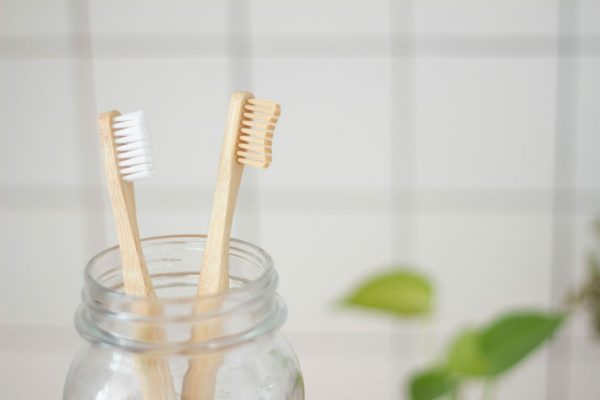 Two toothbrushes sitting in a glass jar with a plant in the background